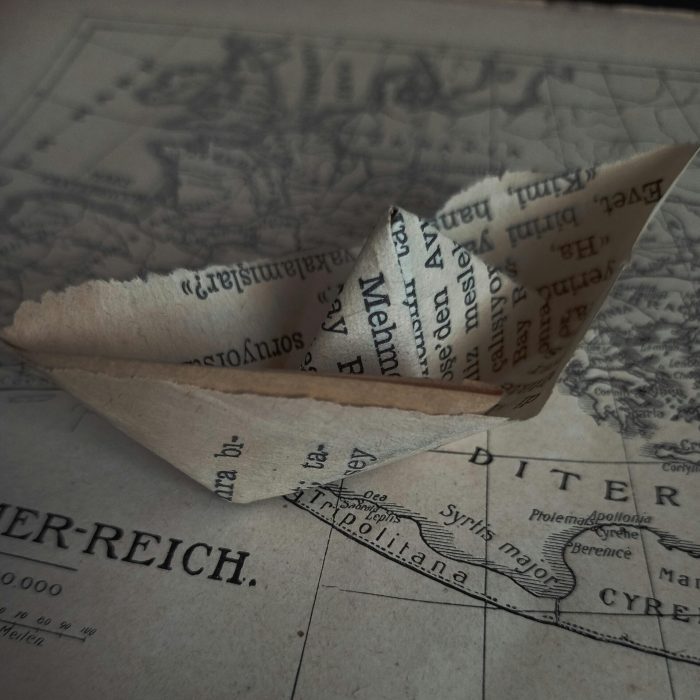 An origami paper ship crafted from text-covered paper rests on a vintage map.